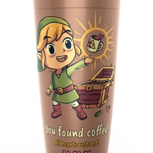 May include: A brown travel mug with a cartoon image of Link from the Legend of Zelda video game series. Link is holding a cup of coffee and the text "You found coffee! All hearts restored!" is printed below the image.