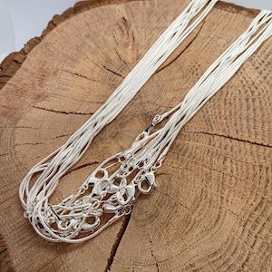 May include: A collection of multiple silver-coloured snake chain necklaces, each featuring a lobster claw clasp. The chains are thin, flexible, and have a smooth, metallic finish, bundled together to show their uniform design and reflective surface.