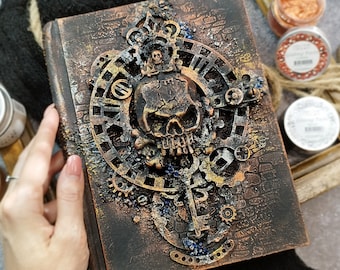 May include: A dark brown leather-bound journal with a skull and gears design. The journal has a distressed, aged look with metallic accents.