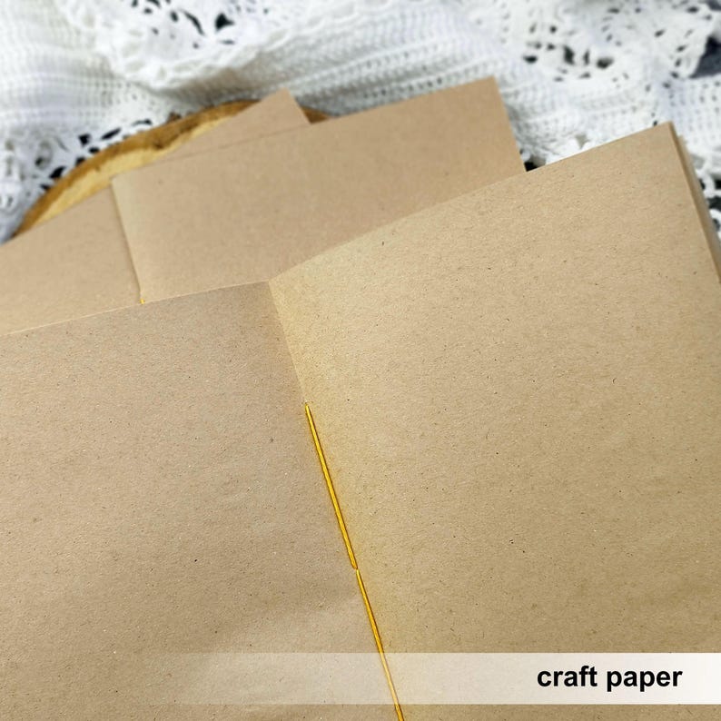 An open kraft paper notebook displays its smooth blank pages and central yellow stitching. This custom sketchbook provides a great foundation for detailed mixed media art.