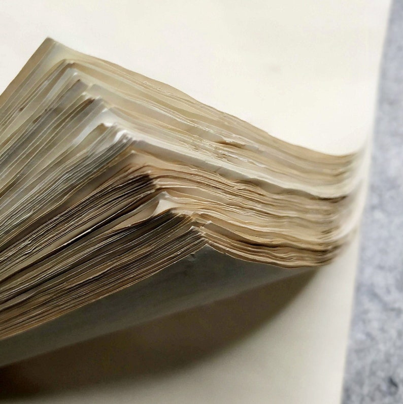 A close-up of a stack of old, yellowed paper pages, showing the edges of the pages and the texture of the paper.