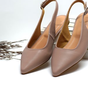 Peut inclure: Une paire de chaussures à bride arrière en cuir marron clair avec des bouts pointus. Les chaussures sont sur une surface blanche.