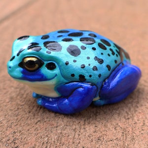 May include: A small blue and black frog figurine with a glossy finish. The frog has black spots on its back and blue limbs.
