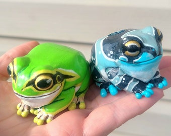 Puede incluir: Dos figuritas de rana pintadas a mano, una verde con marcas negras y la otra azul con marcas negras y blancas.