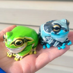 May include: Two hand-painted frog figurines, one green with black markings and the other blue with black and white markings.