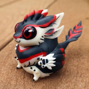 May include: A small, black and red creature with white accents. It has large, round eyes and a feathery tail. The creature is made of polymer clay and is a handmade figurine.