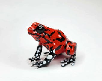 May include: A vibrant red frog figurine with black markings and white spots on its legs. The frog has black eyes and is set against a plain white background. This decorative frog is a unique piece of home decor.