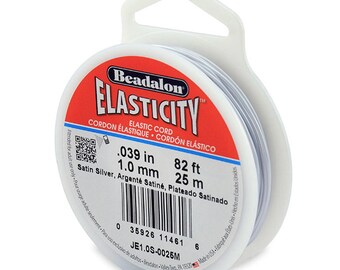 May include: A spool of Beadalon Elasticity elastic cord in satin silver. The spool is labeled with the size, 0.039 inches or 1.0 mm, and the length, 82 feet or 25 meters. The spool is packaged in a clear plastic container with a hanging hole.