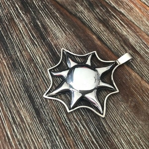 May include: A silver sun pendant with a detailed design. The pendant has a smooth, reflective surface and a loop for attaching a chain.