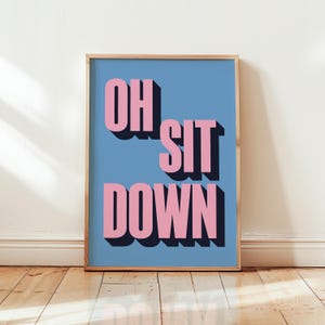 Könnte beinhalten: Ein gerahmter Druck mit blauem Hintergrund und rosa Schriftzug "OH SIT DOWN".