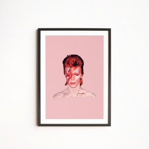 May include: A framed print of a portrait of David Bowie with a red and blue lightning bolt painted across his face. The background is a light pink color.