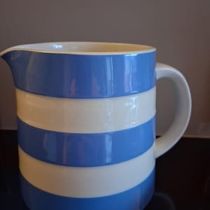 Puede incluir: Una jarra de cerámica con interior blanco y exterior a rayas azules y blancas. La jarra tiene un asa curva y un pico vertedor. El diseño es sencillo y clásico, adecuado para servir bebidas.