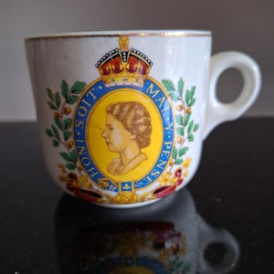 Op de afbeelding: Witte theekop van keramiek met een gouden rand en een blauw en geel koninklijk wapen met een portret van koningin Elizabeth II. Het wapen bevat de tekst "HONI SOIT QUI MAL Y PENSE".