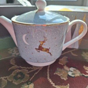 May include: A blue and gold teapot with a reindeer and crescent moon design. The teapot has a lid and a handle.
