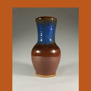 May include: A brown and blue ceramic vase with a speckled glaze. The vase has a wide base and a narrow neck.