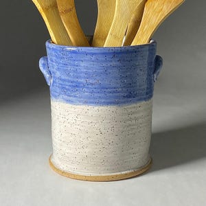 May include: A blue and white ceramic utensil holder with two handles. The holder is filled with wooden spoons.