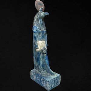 Puede incluir: Una estatua azul y blanca del dios egipcio Horus, de pie sobre una base con jeroglíficos. La estatua está hecha de piedra y tiene cabeza de halcón.