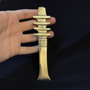 Puede incluir: Una escultura de metal de color dorado que representa una pagoda con un mango largo y delgado. La escultura mide aproximadamente 25 cm de alto y tiene un diseño detallado.
