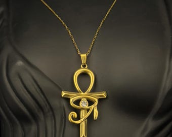 Op de afbeelding: Een gouden ketting met een ankh-hanger met een helder kristal oog van Horus.