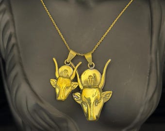 May include: A gold chain necklace with two gold bull head pendants. The bull heads are detailed and have a textured finish.