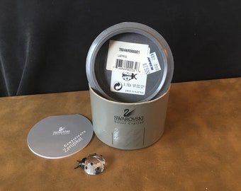 May include: A silver crystal ladybug figurine in a gray box with a certificate of authenticity. The box has a label with the text "7504NR000001 LADYBUG" and a price tag that says "$12.500".