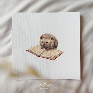 Puede incluir: Pintura a la acuarela de un pequeño erizo sentado sobre un libro abierto. El libro tiene páginas de color beige envejecido y una cubierta roja. El erizo es marrón y gris. El texto "delicate aesthetic" está en la parte inferior.