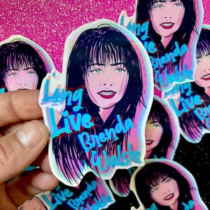 May include: A holographic sticker with a cartoon illustration of a woman with black hair and blue eyes. The text "Long Live Brenda Walsh" is written in blue and pink letters.