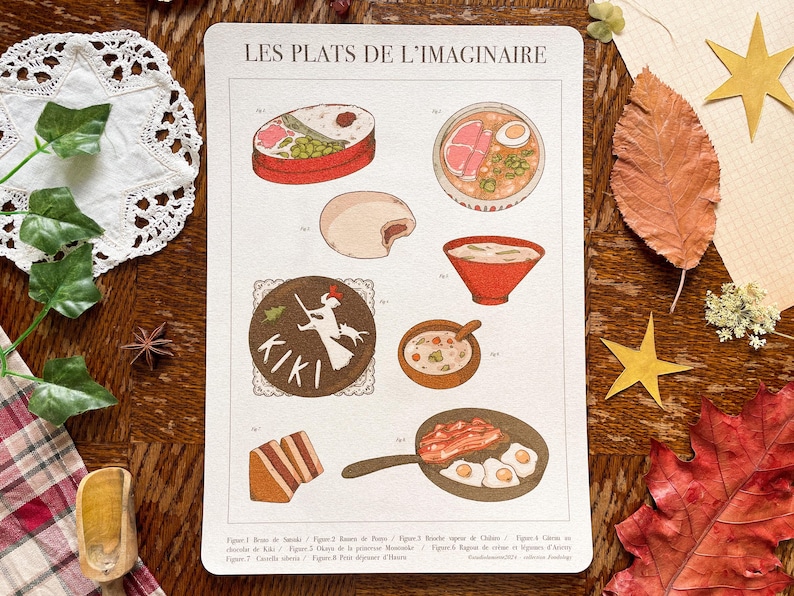 May include: A vintage-style print titled "Les Plats de l'Imaginaire" featuring illustrations of various dishes, including ramen, eggs with bacon, and a round illustration with the text "KIKI". The print is on a cream-colored background with a wooden table.