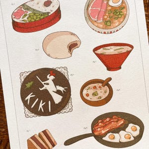 May include: An illustrated print featuring various food items. The print includes a bento box, ramen, a steamed bun, soup in a red bowl, a bowl of soup with a spoon, a pan of bacon and eggs, and a Kiki's Delivery Service themed dessert.