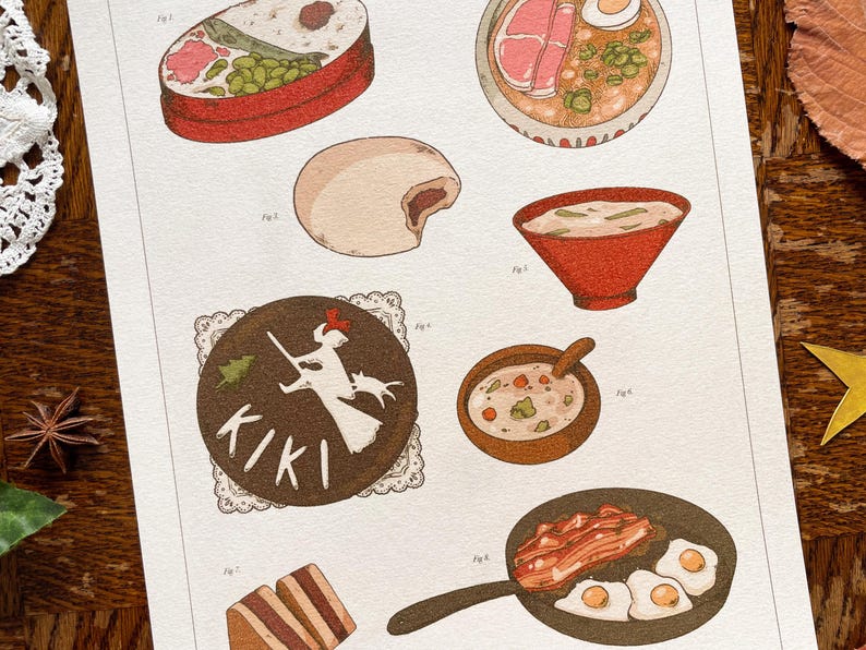 May include: An illustrated print featuring various food items. The print includes a bento box, ramen, a steamed bun, soup in a red bowl, a bowl of soup with a spoon, a pan of bacon and eggs, and a Kiki's Delivery Service themed dessert.