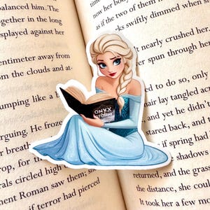 May include: A sticker featuring a cartoon illustration of a woman with long blonde hair, wearing a blue dress, sitting and reading a book titled "Onyx Storm".