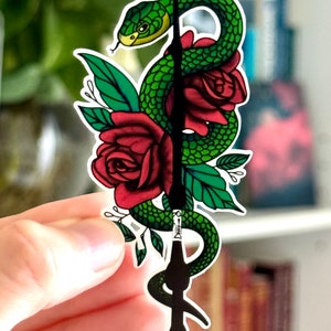 May include: A green snake wrapped around a black wand with red roses and green leaves. The wand has a silver band with a snake design.