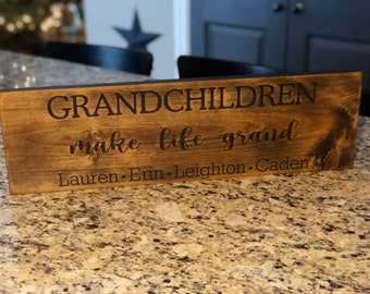 May include: A wooden sign with the text "Grandchildren make life grand" and the names "Lauren, Erin, Leighton, Caden" written below.