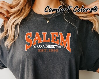 May include: A dark gray t-shirt with an orange graphic that says "Salem Massachusetts Est. 1692" and the words "Comfort Colors" in the top right corner.