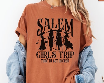 May include: A rust-colored t-shirt with a black graphic of three witches and the text "Salem Girls Trip Time to Get Wicked".