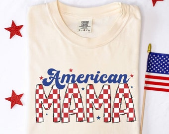 May include: A cream-colored t-shirt with the text "American Mama" in blue and red checkered print. The text is in a retro font style with stars around it.