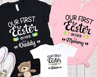 May include: Three matching shirts for a family celebrating their first Easter. A black shirt with the text "Our First Easter 2022 Daddy", a pink shirt with the text "Our First Easter 2022 Mommy", and a white onesie with the text "Our First Easter 2022 Jason".