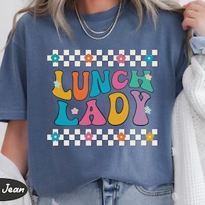 May include: A blue t-shirt with a checkered border and the text "Lunch Lady" in colorful, retro-style letters.
