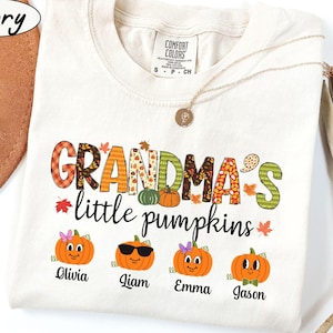 May include: Ivory t-shirt with the text "Grandma's little pumpkins" in colorful patchwork letters. Four smiling pumpkins with names Olivia, Liam, Emma, and Jason are below the text.