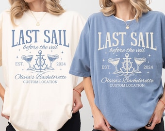 May include: Ivory and blue jean t-shirts with the text "LAST SAIL before the veil" and "Olivia's Bachelorette CUSTOM LOCATION 2024". The design includes an anchor, cocktails, and stars. The shirts are a relaxed fit.