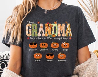 May include: A dark gray heather t-shirt featuring the text This GRANDMA loves her little pumpkins. The design includes seven illustrated orange pumpkins with faces and names underneath, including Greyson, Jackson, Avery, Paige, Gavin, Owen, and Madison.