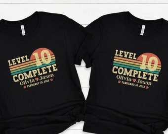 May include: Two black t-shirts with a retro-style graphic that says "Level 10 Complete" with a heart and the names Olivia and Jason and the date February 10, 2013.