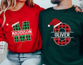 May include: Red and green Christmas themed sweatshirts with the letters "M" and "O" decorated with buffalo plaid and a Santa hat. The name "MADDISON" is written below the "M" and the name "OLIVER" is written below the "O".