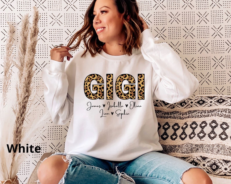 May include: White sweatshirt with the word "GIGI" in leopard print letters. Below the word are the names "James", "Isabella", "Olivia", "Liam", and "Sophia" with hearts between each name.