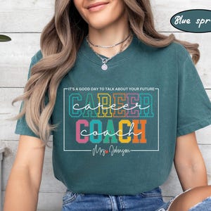 May include: A teal blue t-shirt with the text "It's a good day to talk about your future" above the words "career coach" in colourful block letters. The text "Mrs. Johnson" is below the words "career coach".