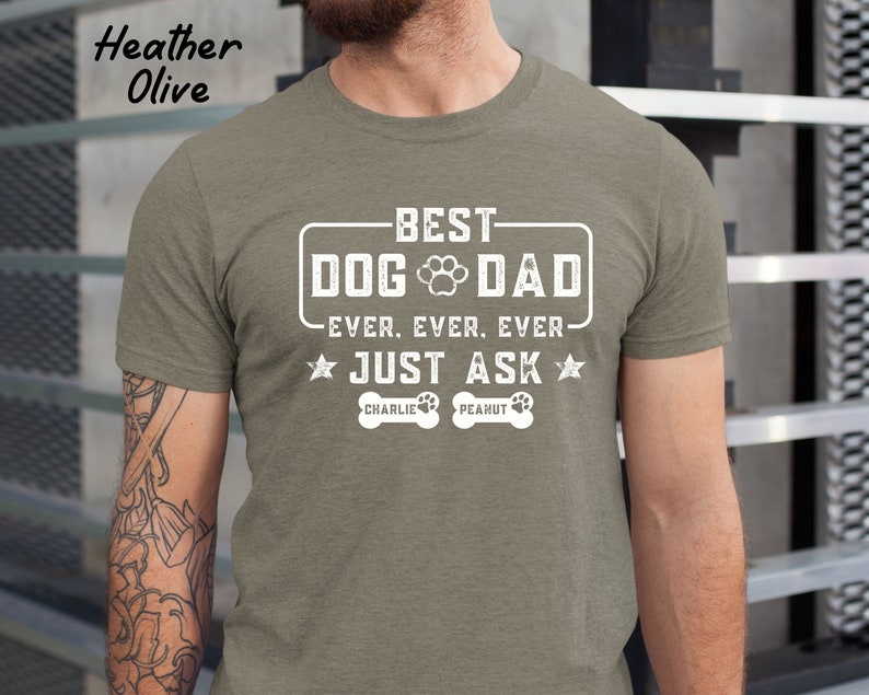 May include: Heather olive t-shirt with the text "BEST DOG DAD EVER. EVER. EVER. JUST ASK" in white. The shirt also features a paw print and the names "Charlie" and "Peanut" below the text.
