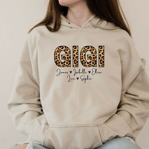 May include: A beige hoodie with a leopard print "GIGI" design and the names "James, Isabella, Olivia, Liam, Sophie" written below in black.