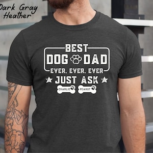 May include: Dark gray heather t-shirt with the text "BEST DOG DAD EVER. EVER. EVER. JUST ASK" in white. The design includes a paw print and two stars. The names "Charlie" and "Peanut" are printed below the text.