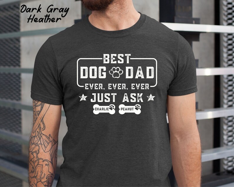 May include: Dark gray heather t-shirt with the text "BEST DOG DAD EVER. EVER. EVER. JUST ASK" in white. The design includes a paw print and two stars. The names "Charlie" and "Peanut" are printed below the text.