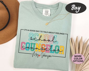 Puede incluir: Una camiseta azul claro con el texto "It's a good day to talk about feelings - school counselor - Mrs. Johnson" en letras mayúsculas de colores.